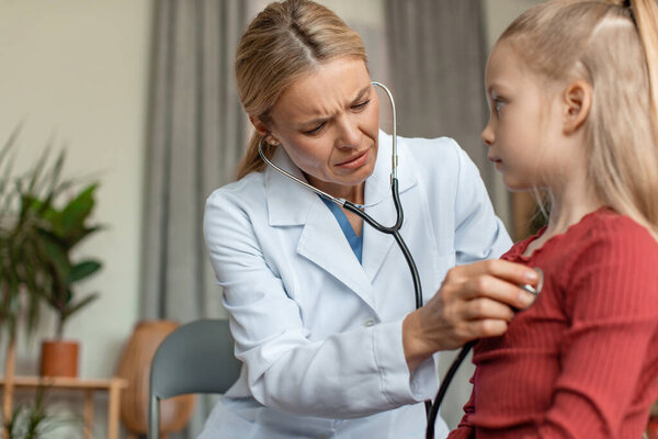 Worried pediatrician doctor examining little girls heart beat and lungs with stethoscope, doing pediatric checkup, child having problems