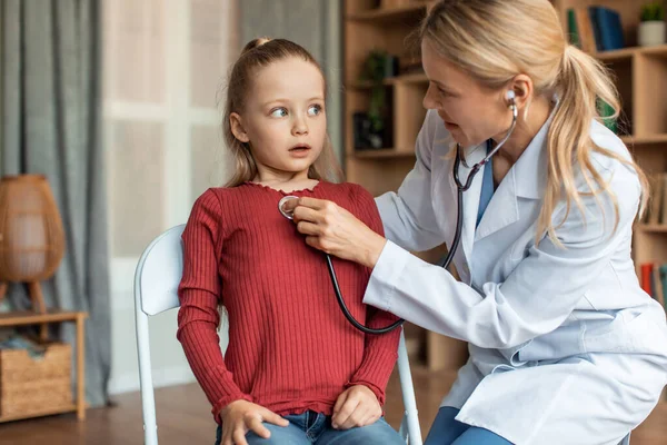 Professional kids medicare. Female pediatrician listening little scared girl heart beating with stethoscope, checking up health condition at home, having domestic visit