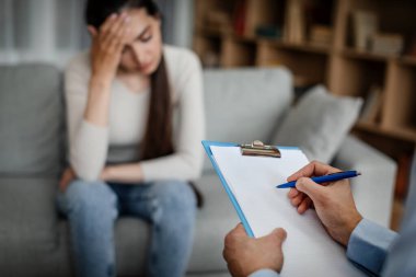 Despaired european young woman patient is sad at consultation, male doctor makes notes in clinic interior, selective focus, cropped. Mental treatment and support, patient care, psychological problems