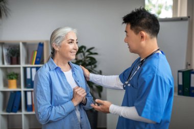 Ofis kliniğinde üniformalı bin yıllık Japon doktor sayesinde buluşmadaki yaşlı, mutlu beyaz kadın hasta. Emekli olma, sağlık danışmanlığı, profesyonel terapistle tedavi