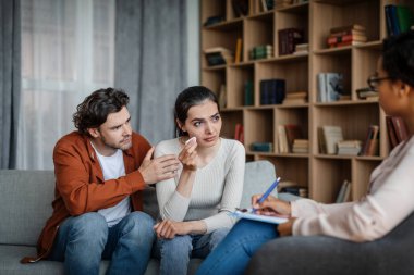 Unhappy sad millennial caucasian man calms crying woman at meeting with psychologist in office clinic interior. Psychological therapy, family session with professional, people emotions and depression