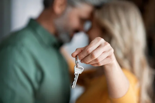 Closeup Shot Of Romantic Middle Aged Couple Holding Home Keys, Loving Mature Spouses Celebrating Moving To Their Own House, Embracing And Touching Foreheads, Cropped Image With Selective Focus