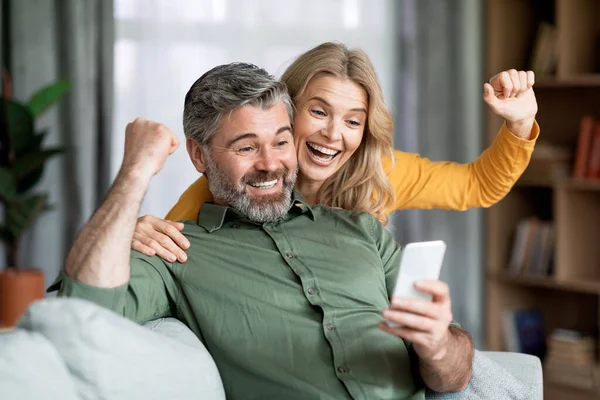 Excited Middle Aged Couple Celebrating Success While Looking Smartphone Screen — Stockfoto