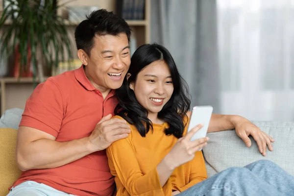 Cheerful Chinese Lovers Man Woman Homewear Sitting Couch Using Smartphone — стокове фото