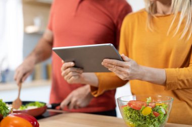 Unrecognizable couple cooking healthy dinner or lunch together at home, checking recipes online, using digital tablet, reading culinary blog on Internet, cropped, copy space