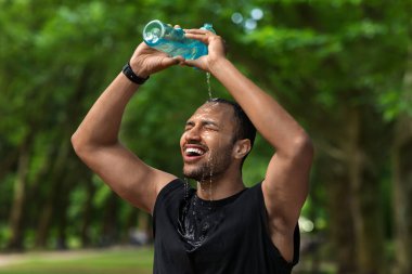 Hot african american young guy sportsman splashing water on his head, cooling down while running by public park in summer, sportsman preparing for marathon, copy space, closeup shot