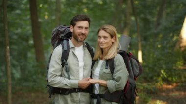 Active family hobby. Outdoor portrait of happy loving middle aged couple in love with backpack hugging in forest, enjoying hiking trip together, smiling to each other, slow motion