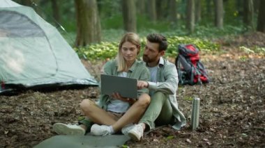 Internet and nature. Happy middle aged spouses resting at camping and web surfing online on laptop, bonding outdoors near tent, slow motion, free space