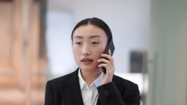 Mobile communication. Close up portrait of positive asian woman in formal wear talking with colleagues on cellphone, discussing project details at office, slow motion
