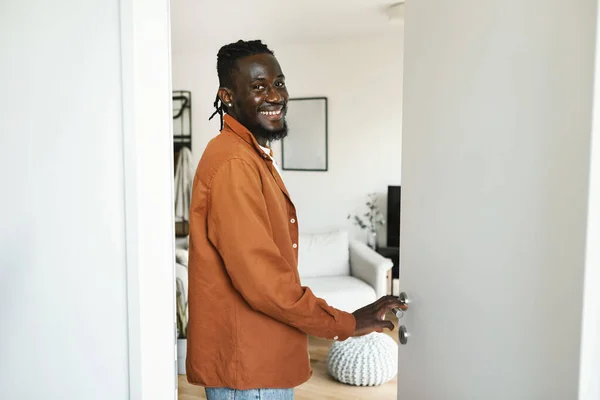 Welcome to my home. Cheerful black man walking in his apartment, entering new home and looking back at camera, happy male standing in doorway of modern flat