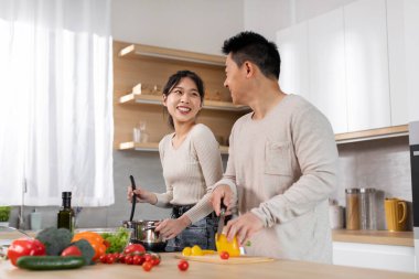 Pozitif Japon orta yaşlı koca ve genç karısı evde lezzetli sağlıklı bir akşam yemeği yapıyorlar, sohbet ediyorlar ve gülümsüyorlar, birlikte eğleniyorlar, beyaz mutfak içleri, kopyalama alanı.