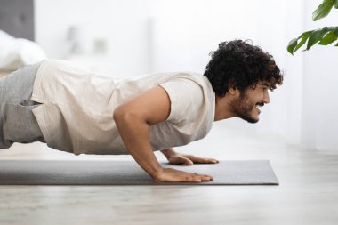 Spor giyimli, spor kıyafetli, spor kıyafetli, Hintli bir adam sabah yoga antrenmanı yapıyor, reklam için fotokopi odasına bakıyor, yatak odası içi, yan görüş.
