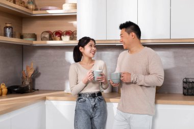 Pozitif Çinli eşler güzel genç kadın ve neşeli orta yaşlı adam birlikte vakit geçiriyorlar, beyaz rahat mutfakta kahve içiyorlar, sohbet ediyorlar ve gülümsüyorlar.