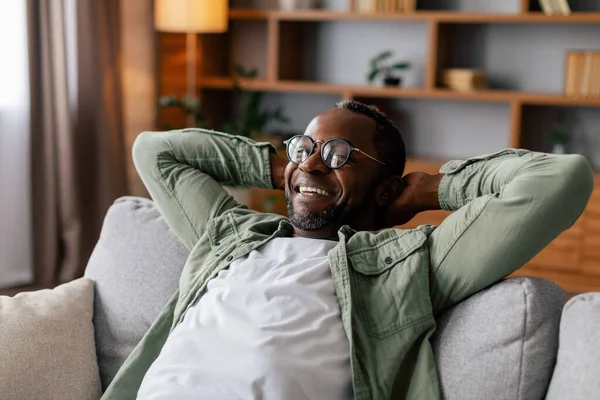 心满意足的非洲裔美国成年人 戴着眼镜 悠闲自在地休息和放松 独自在客厅里享受着舒适 宁静和闲暇的时光 在Covid 19检疫期间在舒适的家休息一下 — 图库照片