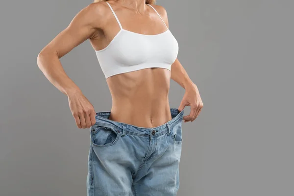 Successful diet concept. Cropped shot of young female in big size jeans demonstrating results of her slimming program, unrecognizable woman in oversize clothes comparing body after weight loss