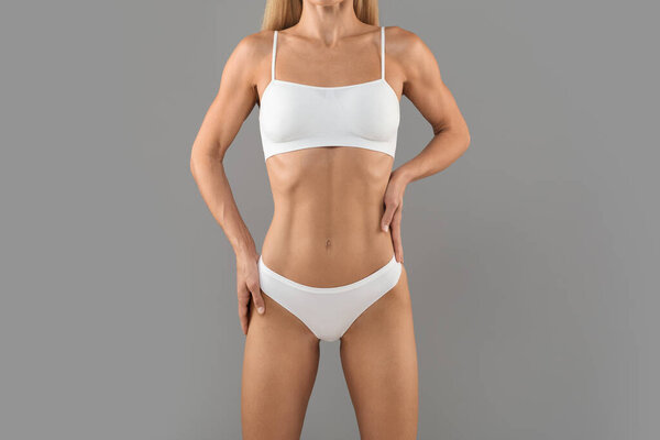 Обрезанный вид спереди стройная женщина с идеальным телом и плоский желудок Поза изолированы на сером фоне студии, неузнаваемая женщина с подходящей фигурой носить белый лифчик и трусики, скопировать пространство