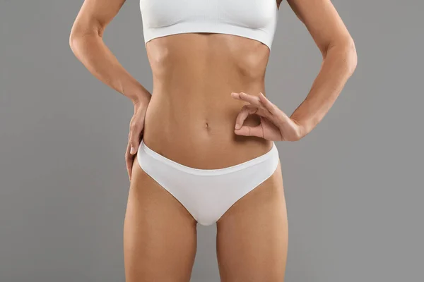 Woman Health. Young slim woman wearing white underwear showing ok gesture while standing isolated on grey studio background, unrecognizable female with perfect body gesturing sign of approval