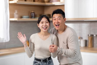 Mutlu evli Asyalı eşler, rahat beyaz mutfakta şarkı söylüyor mutfak gereçlerini mikrofon olarak kullanıyor, güzel genç bayan, sevgi dolu orta yaşlı kocasıyla evde vakit geçiriyor, uzay fotokopisini çekiyor.