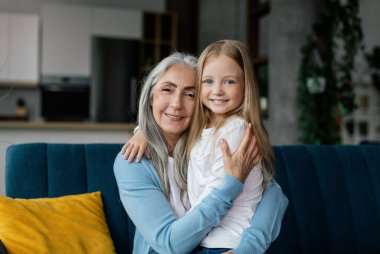 Aşk ve aile ilişkisi. Mutlu Avrupalı yaşlı büyükanne ve küçük torun kucaklaşmaları oturma odasının içinde birlikte boş vakit geçirmeleri. İnsani duygular, evdeki yaşam tarzı, covid-19