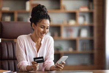 Ofiste mola verirken internetten alışveriş yapan neşeli genç bir bayan cep telefonu ve limitsiz kredi kartı kullanıyor çalışırken internetten bir şeyler alıyor, yer kopyalıyor. E-ticaret kavramı