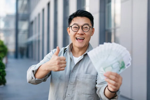 Alegre Empresario Asiático Sosteniendo Ventilador Euro Dinero Mostrando Pulgar Hacia — Foto de Stock