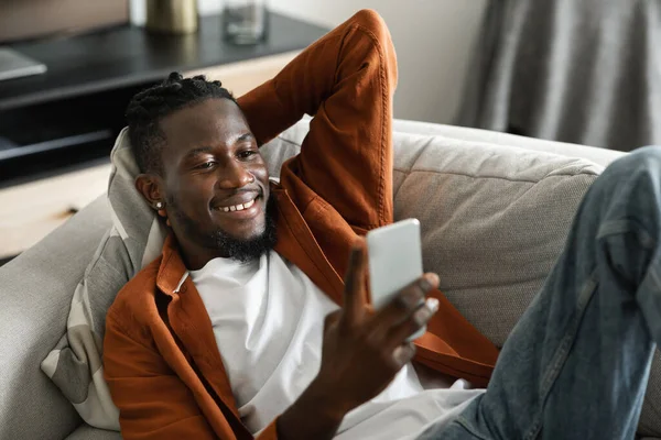 快乐的非洲裔美国人在智能手机上看视频 在客厅的沙发上休息和放松 视频通话 新的应用程序 在线提供和技术在家里 — 图库照片