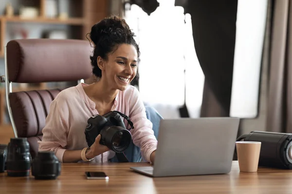 Jobs and occupations for millennials concept. Creative attractive brunette young lady photographer enjoying her job, holding professional camera, checking photos on laptop, office interior, copy space