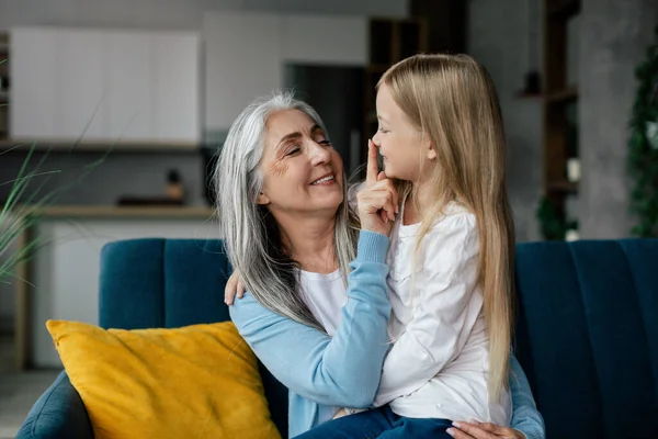 笑笑的欧洲老奶奶抱着小孙女 触摸着鼻子 享受着在客厅里的闲暇时光 爱情和家庭关系 人们的情感 家里的生活方式 — 图库照片