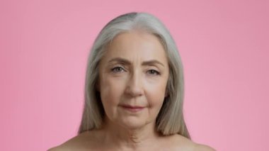 Yaşlanmanın güzelliği. Kameraya bakan, yaşlı, güzel, kır saçlı, kırışık, pembe stüdyo geçmişi olan bir kadının portresini yakından çek.