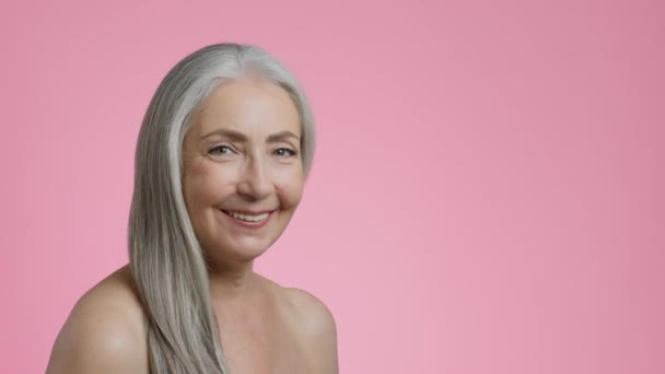 老年妇女高级化妆品广告 工作室的肖像 是快乐的灰白头发女士 光秃秃的肩膀 脸转向相机 面带微笑 粉色背景 空白的文字空间 — 图库视频影像
