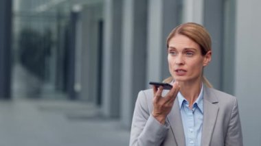 Modern iletişim. Kendine güveni tam orta yaşlı bir iş kadını akıllı telefonuyla konuşuyor, hoparlörle konuşarak sesli mesaj kaydediyor, dışarıda dikiliyor, çekim yapıyor, yavaş çekim yapıyor, boş alan arıyor.