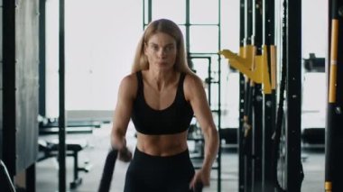Dayanıklılık fonksiyonel eğitim. Spor salonunda halatlarla egzersiz yapan kaslı, güçlü, sportif bir kadının portresi.