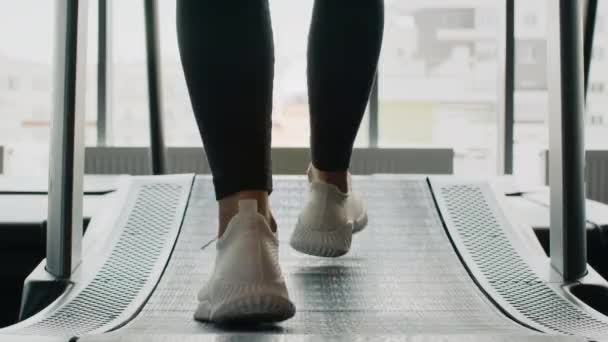 ジョグワークアウト ジムでトレッドミルを歩く白いスニーカーを身に着けている認識できない女性の足のショットを閉じます トレーニング前にウォーミングアップ スローモーション — ストック動画