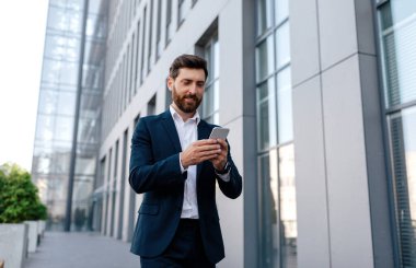 Kendine güveni tam, takım elbiseli, yakışıklı, beyaz bir adam işe gidiyor. Modern ofis binasının yanında akıllı telefonuyla video görüşmesi yapıyor. İş adamı ve yeni iş uygulaması, yeni normal
