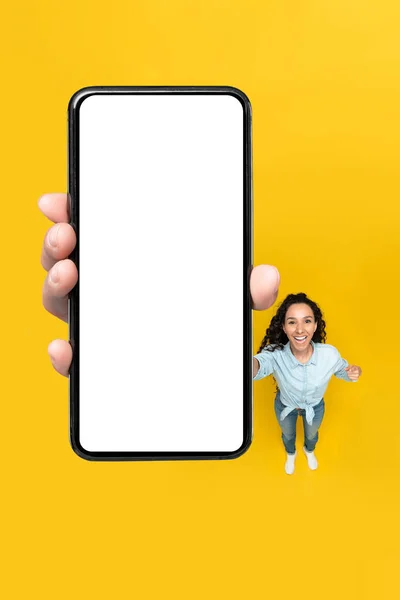 兴奋的中东女性展示手机与巨大空白屏幕广告移动应用站在黄色背景在工作室 检查这个哇应用程序 Top View Mockup — 图库照片