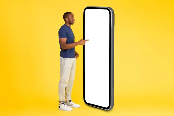 黄色のスタジオの背景に空の画面広告モバイルアプリと大規模なスマートフォンを使用してアフリカ系アメリカ人男性 テクノロジーとガジェットの概念 サイドビュー モックアップ — ストック写真