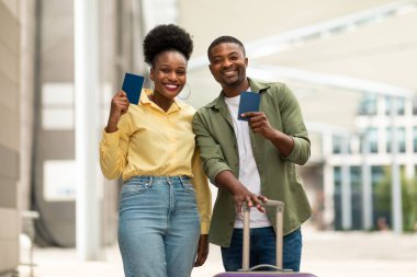 Tatil seyahati. Mutlu Siyah Eşler, Pasaportları Kameraya Gülümseyen Bavul Açık Havalimanı Terminali 'ne yakın bir yerde. Milenyum Turistleri Yurtdışına Birlikte Seyahat Ediyor