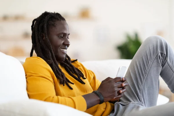 Feliz Joven Negro Mensajería Teléfono Inteligente Mientras Relaja Sofá Casa —  Fotos de Stock