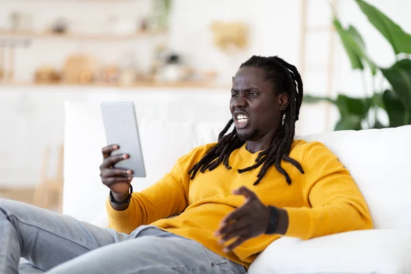 Enojado Joven Negro Hombre Con Tableta Digital Sentado Sofá Sala —  Fotos de Stock