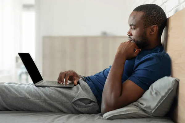 Vista Lateral Del Hombre Negro Usando Ordenador Portátil Sentado Cama —  Fotos de Stock