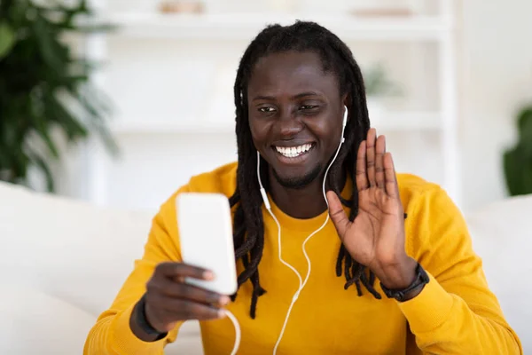 遠隔通信 自宅でビデオ通話のためのスマートフォンを使用して幸せな黒人男性 リビングルームで休憩しながら友人とオンラインチャットを楽しむ陽気な若いアフリカ系アメリカ人の男 スペースをコピー — ストック写真