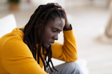 Depresyon Konsepti. Evde yalnız başına oturan üzgün siyah erkek portresi, Kafasına dokunan ve yere bakan, depresyonda hisseden, yakın çekim yapan,
