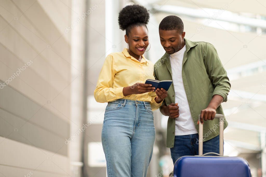 Cheerful African American Tourists Couple Traveling Together Holding Passports With Boarding Passes Standing With Suitcase Outdoors. Vacation Travel Concept