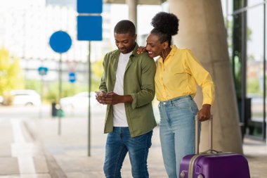 Mobil Uygulamada Cep Telefonu Rezervasyon Uçuşunu kullanan Mutlu Siyah Turistler Havaalanı Terminali 'nin yanında duruyor. Turizm ve Mobil İletişim Konsepti