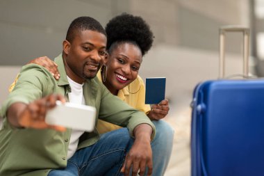 Tatil seyahati. Mutlu Afro-Amerikan turistler havaalanında cep telefonu pozu ve pasaportlarıyla selfie çekiyorlar. Turizm ve Mobil Teknoloji. Seçici Odaklanma