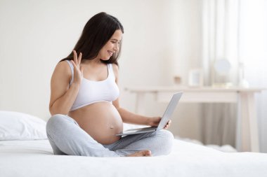 Neşeli, hamile bir bayan evde yatarken dizüstü bilgisayar kullanıyor, doğum izni sırasında online eğitim alıyor, arkadaş, doktor, ekranda el sallıyor, boşluğu kopyalıyor.