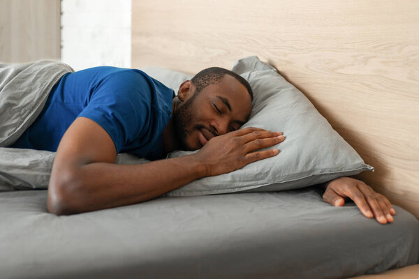 Black Guy Sleeping Peacefully Holding Hands Near Face Lying In Cozy Bed In Modern Bedroom At Home. Millennial Male Napping Resting At Night. Sweet Dreams Concept