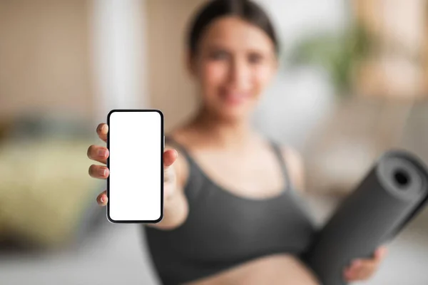 Mobile Ad. Pregnant Woman Holding Smartphone With Blank Screen And Yoga Mat, Smiling Young Expectant Female Recommending New Application Or Website For Trainings During Pregnancy, Mockup