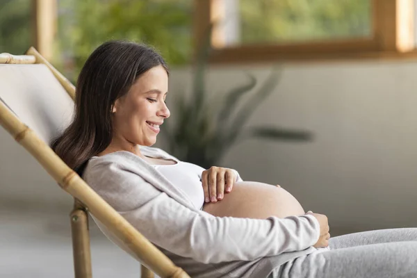 Güzel Gülümseyen Hamile Bir Kadın Evinde Sandalyesinde Dinlenirken Karnına Sarılıyor — Stok fotoğraf