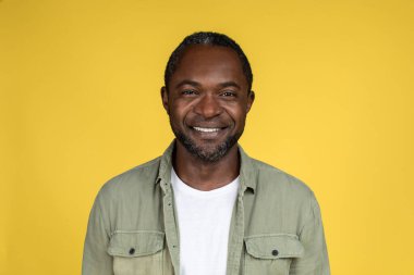 Kendine güvenen Afrikalı Amerikalı bir erkeğin sarı arka planda, stüdyoda, kapalı, kapalı, boş alana baktığı vesikalık fotoğrafı. İnsanların duyguları ve yüz ifadeleri, reklam ve sunum